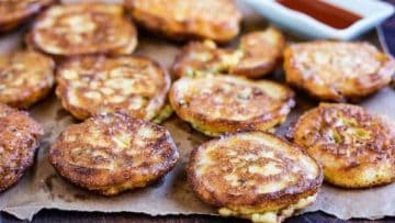 Golden-brown fried green tomato fritters on a parchment-lined tray, with a side of red dipping sauce.