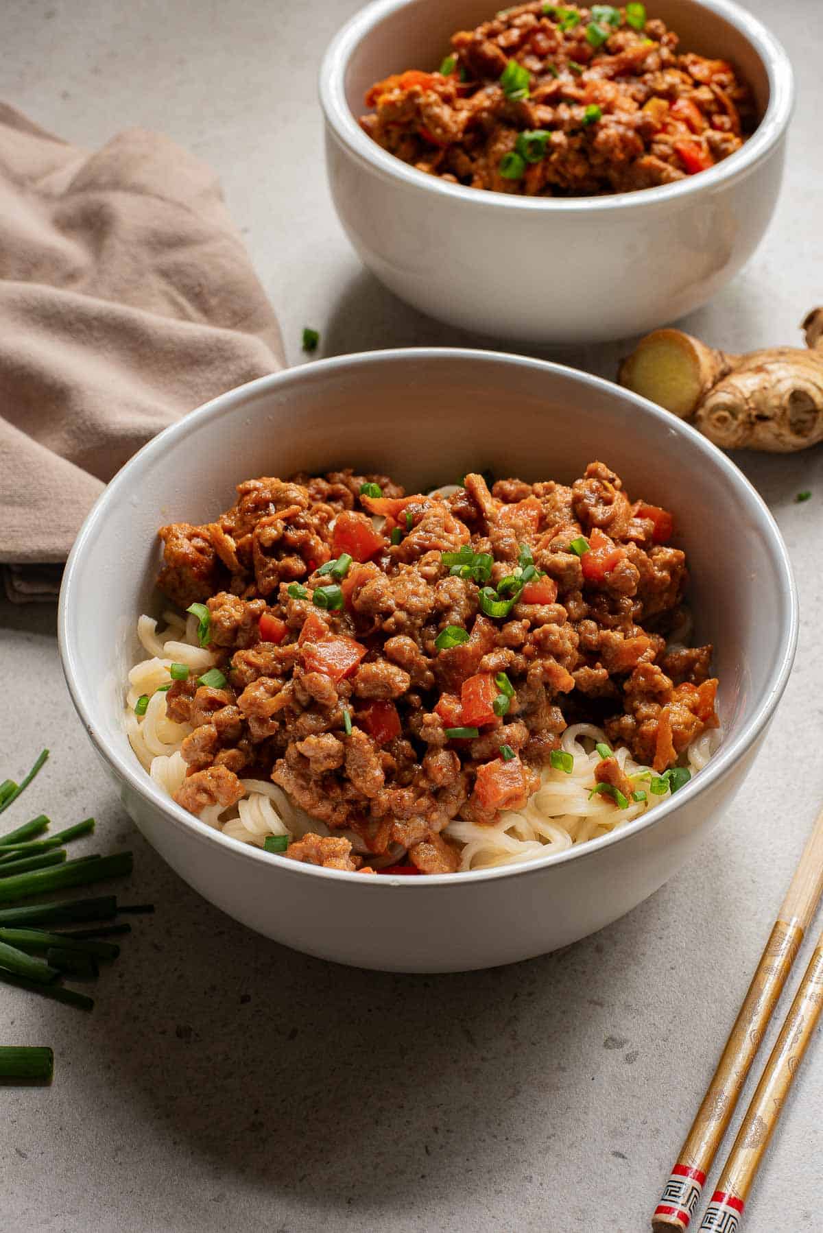 A bowl of noodles topped with peanut sauce beef, garnished with green onions.
