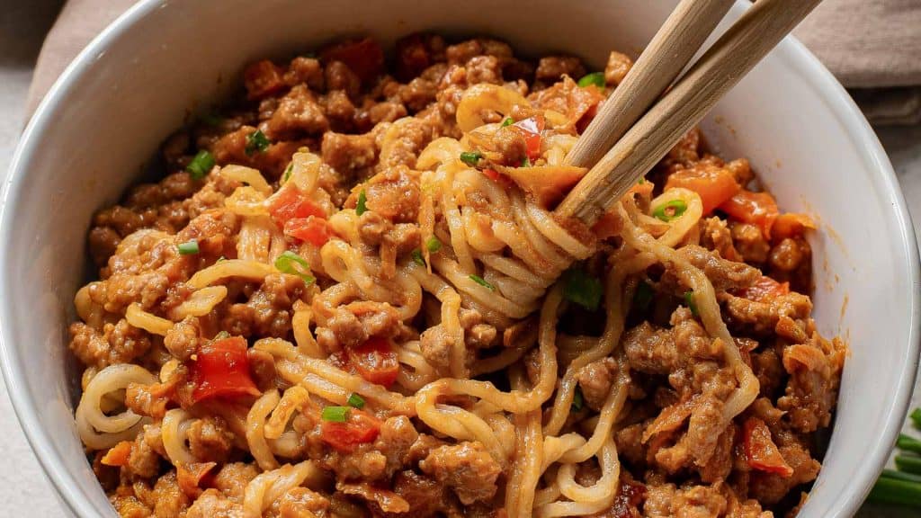 A bowl of spaghetti noodles with a fork twirling noodles, highlighting ground meat and chopped vegetables in the sauce.