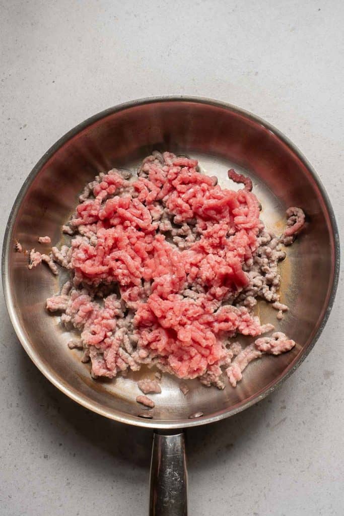 Ground meat partially cooked in a stainless steel frying pan.
