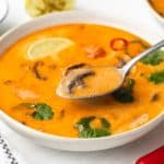 A bowl of creamy soup with mushrooms, herbs, and a touch of lime, served with a spoon.