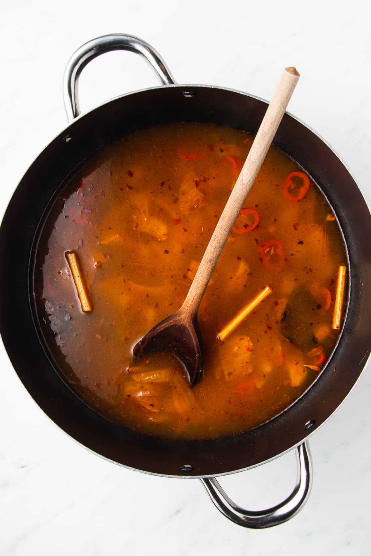 A pot of soup with vegetables and a wooden spoon.