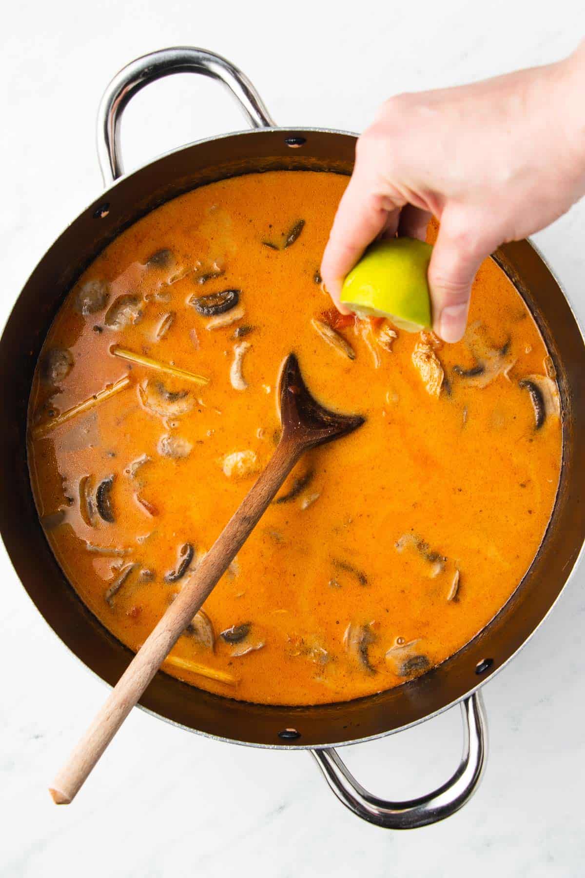 A person's hand squeezing a lime into a pot of soup with mushrooms.