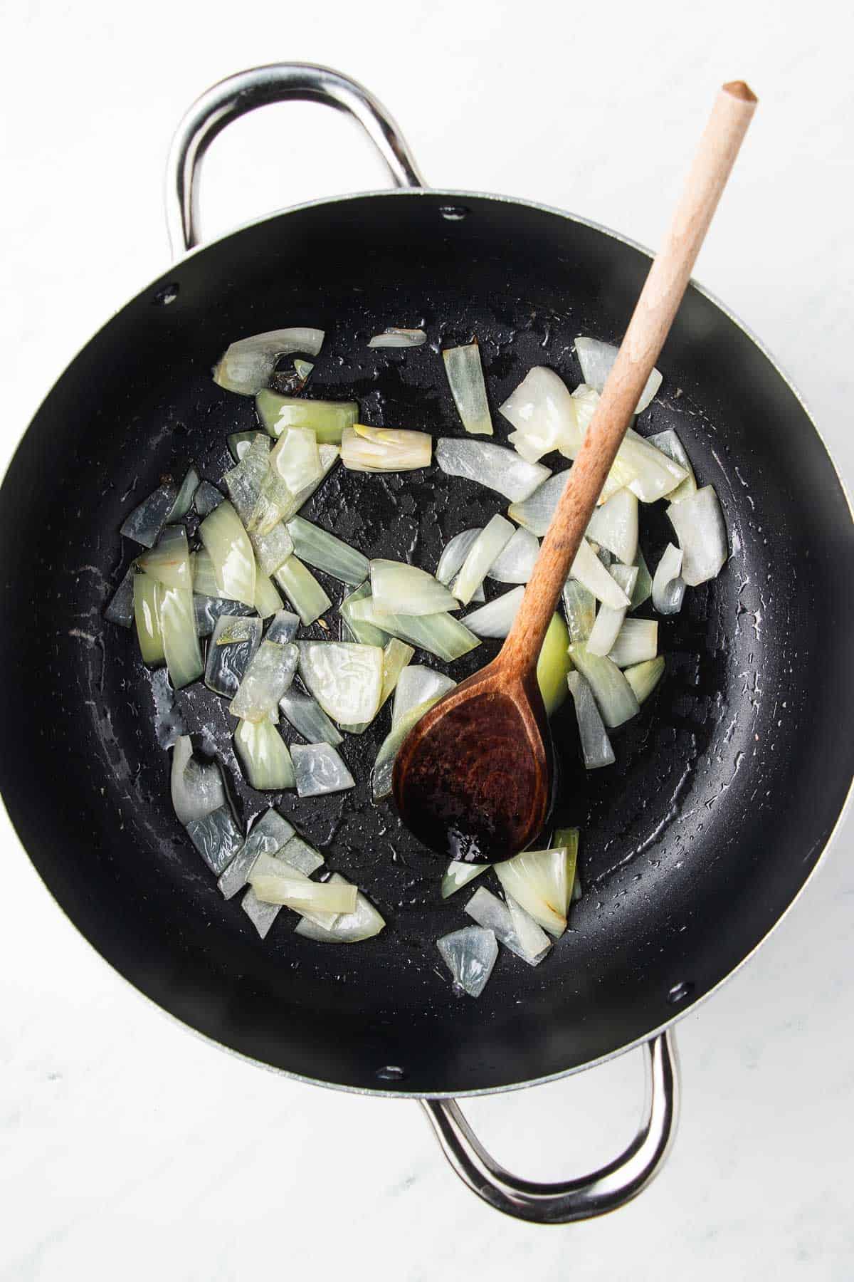 Sautéed onions in a black wok with a wooden spoon.