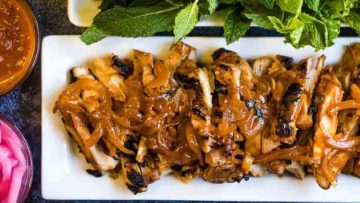Grilled chicken with caramelized onions and herbs on a white plate, served with a side of sauce.