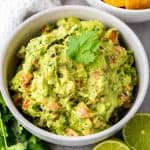 A bowl of guacamole garnished with a cilantro leaf and lime halves.