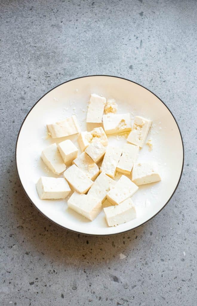 Slices of uncooked tofu on a white plate placed on a grey countertop.