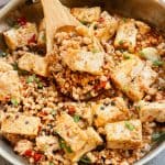 A pan filled with tofu cubes and ground meat mixed with chopped green onions and red chilies, stirred with a wooden spoon.