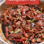 A pan filled with savory Mongolian pork, garnished with sliced green onions, whole dried red chilies, and sesame seeds.