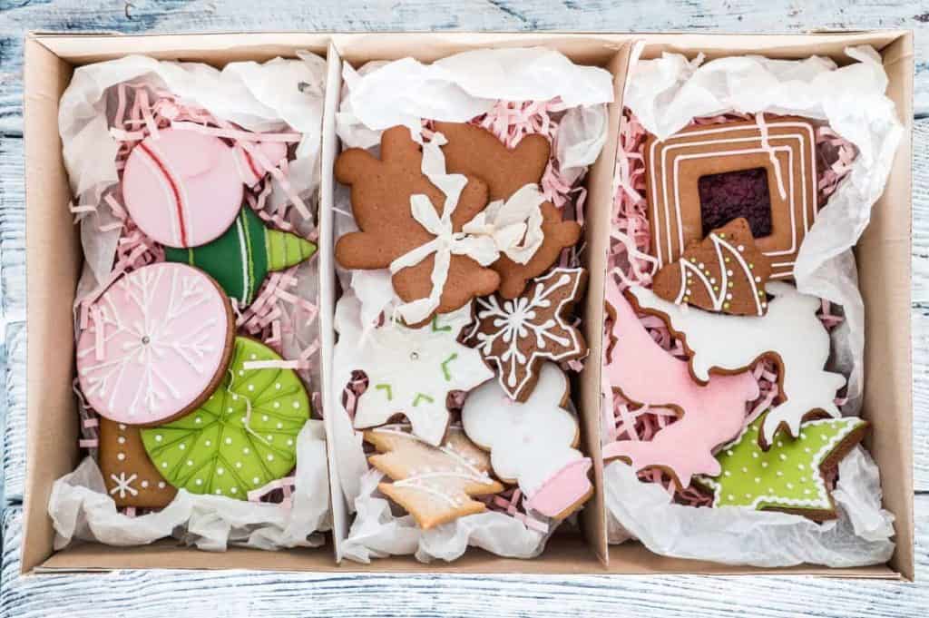 A box of assorted decorated cookies, including gingerbread figures, snowflakes, and geometric shapes, arranged on white tissue paper.