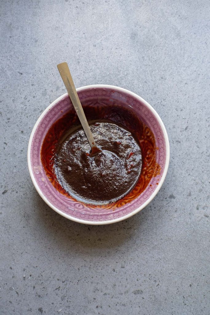 A bowl of dark red sauce with a spoon on a gray countertop.