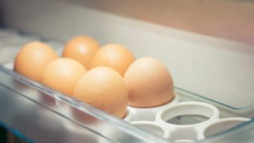 Six brown eggs in a transparent refrigerator egg tray.