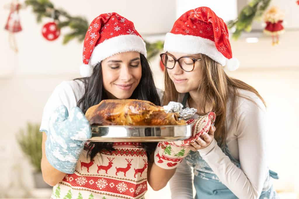 Two people, donning Santa hats and oven mitts, proudly present an easy holiday roasted turkey in a festive kitchen setting.