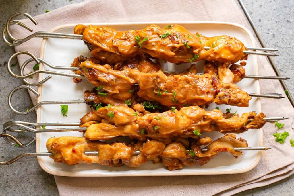 Grilled chicken skewers with sauce and garnished with chopped herbs, served on a rectangular white plate.