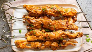 Grilled chicken skewers with a glaze, garnished with chopped herbs, served on a white rectangular plate.