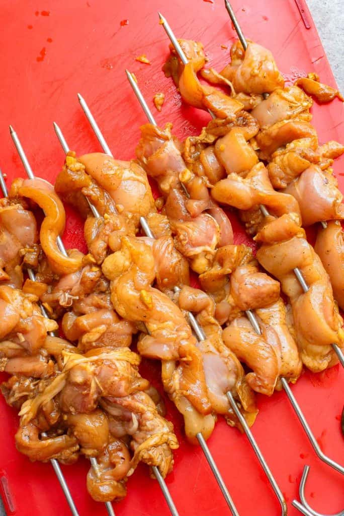 Marinated chicken pieces skewered on metal sticks, placed on a red cutting board.