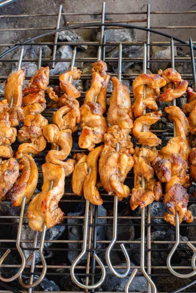 Grilled skewers of marinated meat cooking over charcoal on a barbecue grill.