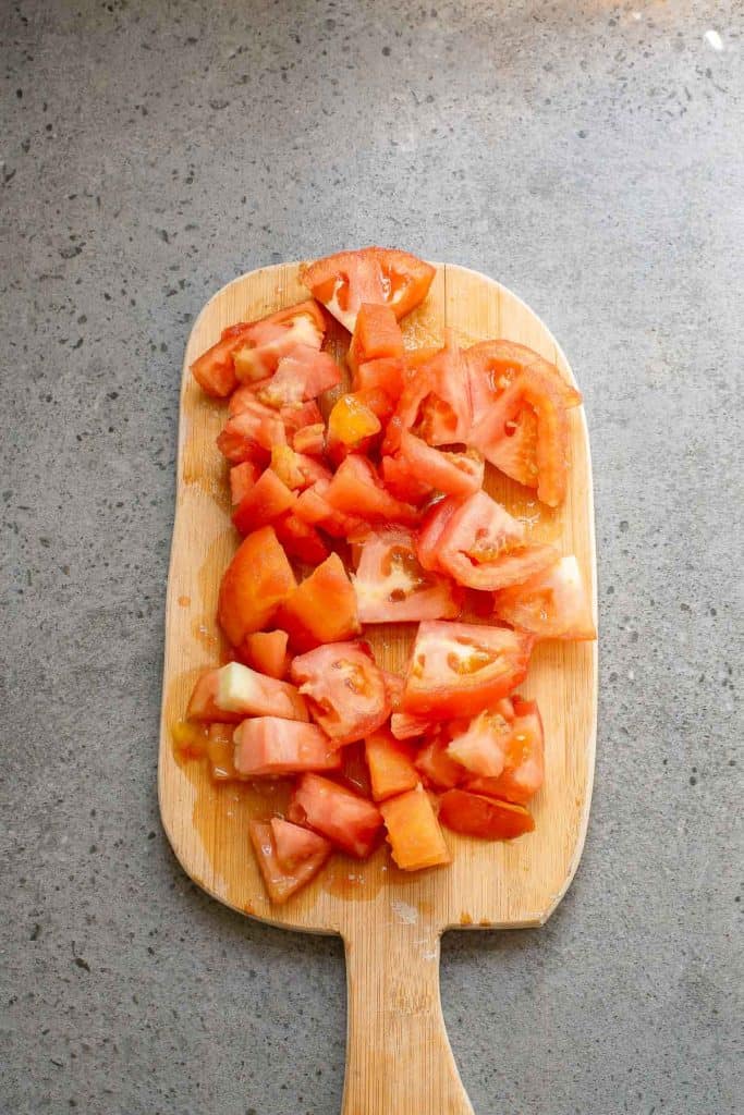 Chopped tomatoes on a wooden cutting board placed on a gray countertop.
