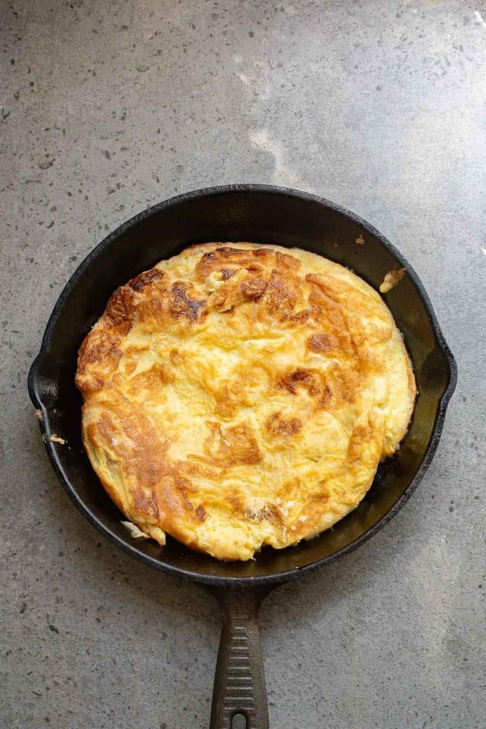 A cooked omelette in a black cast iron skillet on a gray stone surface.