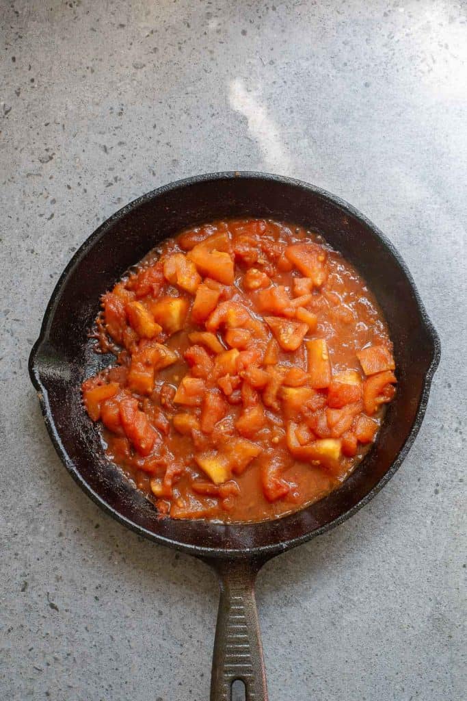 A cast iron skillet containing cooked diced peaches in a sauce, placed on a speckled countertop.