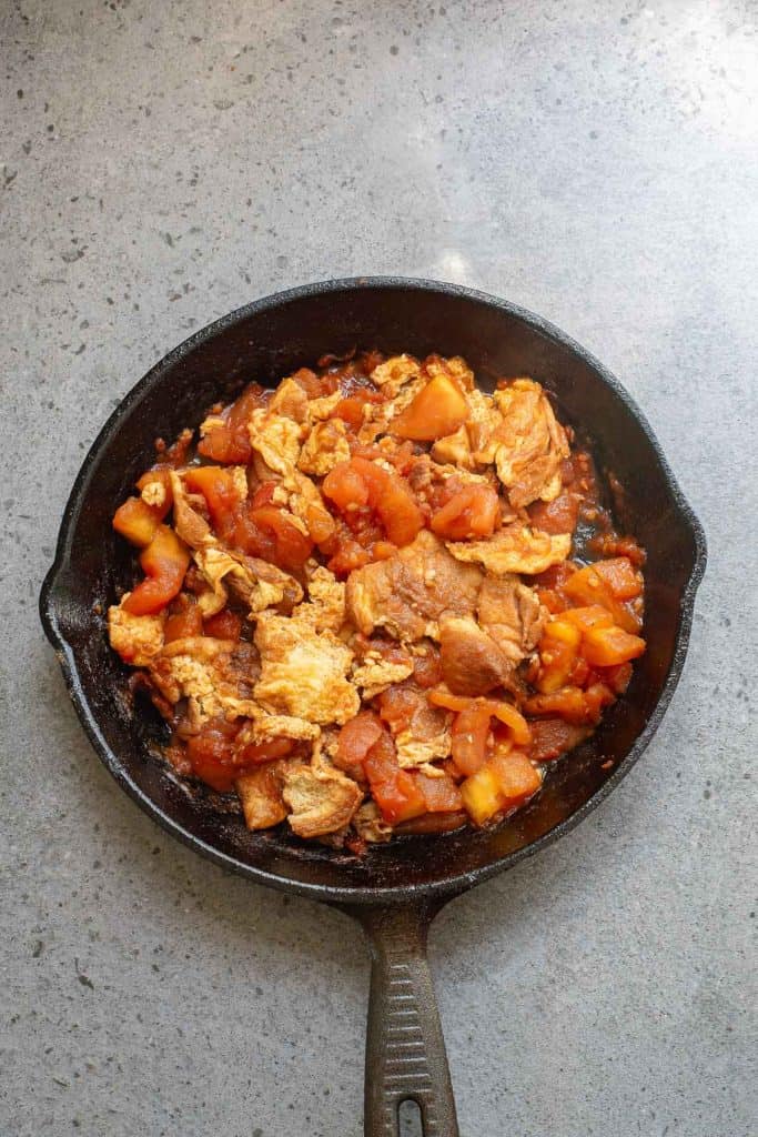 A cast iron skillet containing cooked egg and diced tomatoes, placed on a gray countertop.
