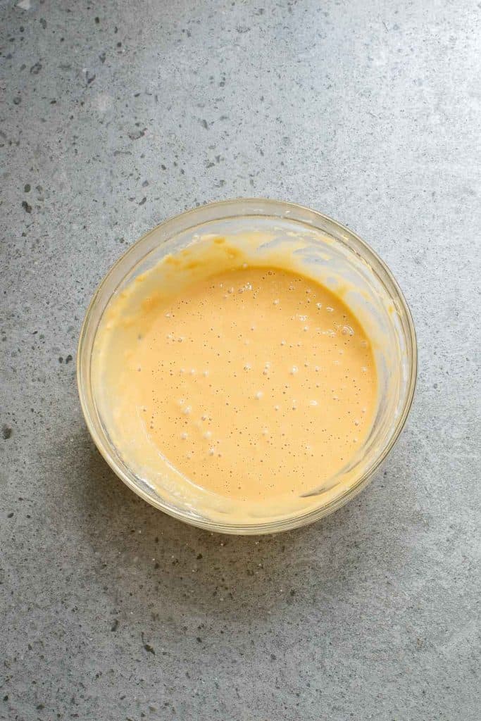 A glass bowl filled with a creamy, light orange batter on a gray countertop.