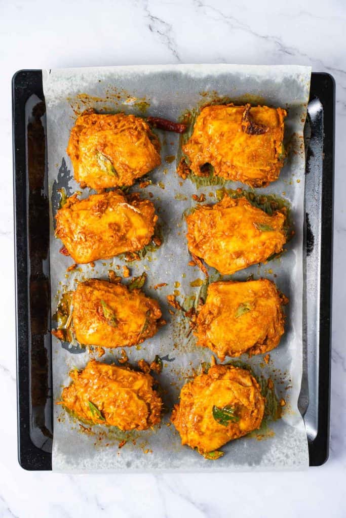 Baking tray lined with parchment paper holding eight pieces of baked, cheese-topped stuffed peppers on a marble surface.