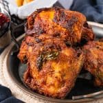 A close-up of several pieces of cooked, marinated chicken on a metal plate, displaying a crispy, seasoned exterior with visible herbs.