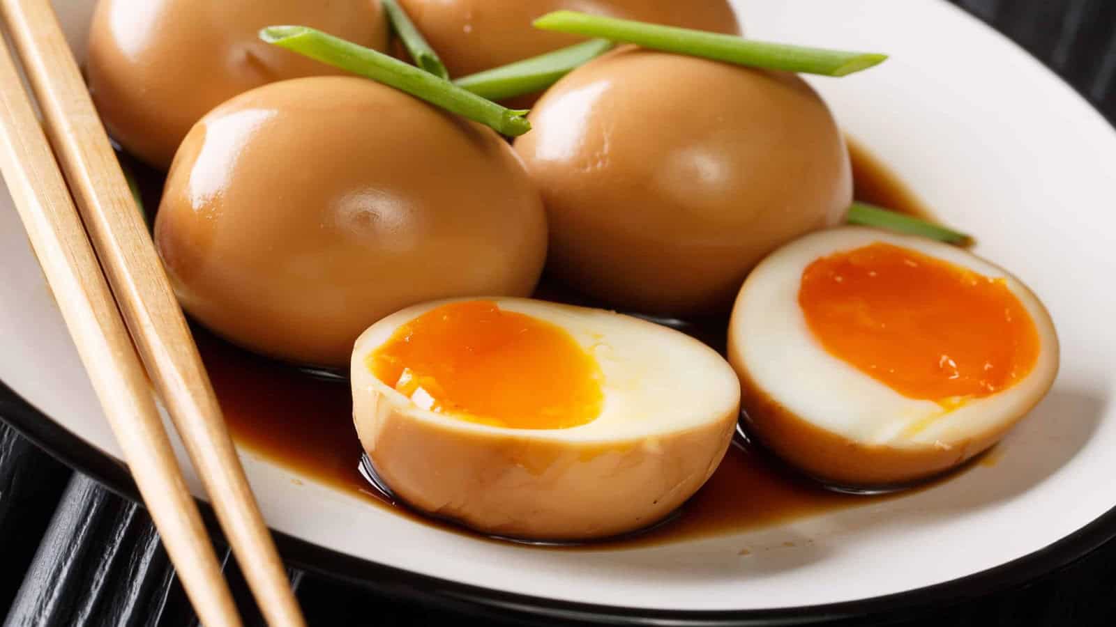 A plate of marinated soft-boiled eggs with runny yolks, garnished with green onions, next to a pair of chopsticks.