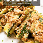 Sliced cucumbers topped with a chunky peanut dressing and crushed peanuts on a white plate.