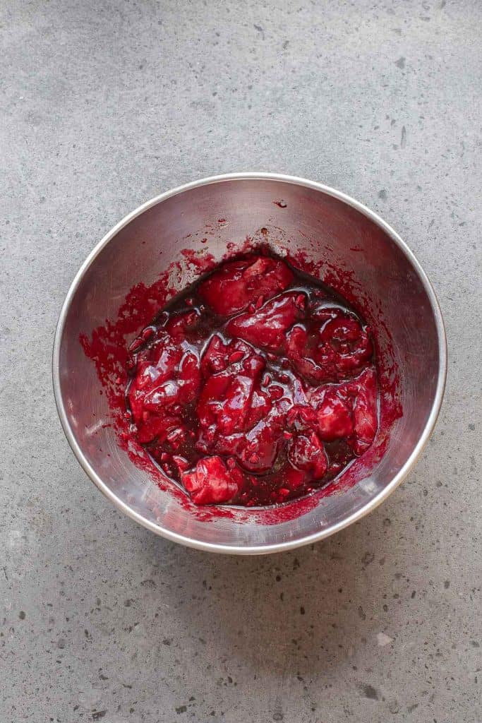 A stainless steel bowl containing a mixture of chopped red fruit and juice on a gray countertop.