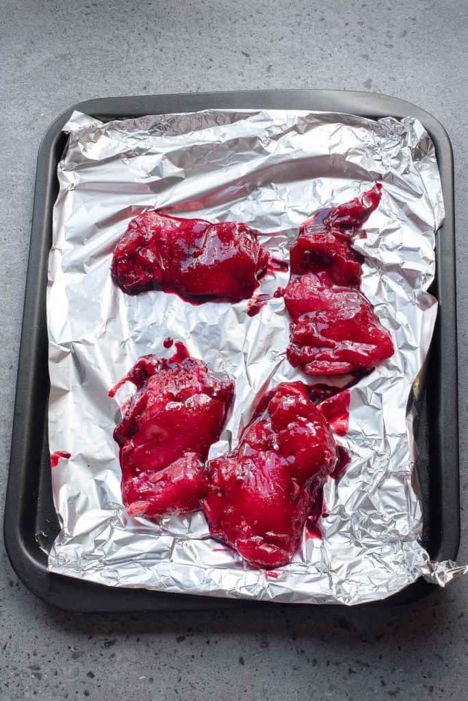 Raw liver pieces are placed on a foil-lined baking tray, ready for cooking, on a gray countertop.