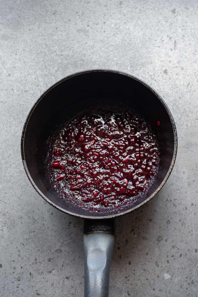 A small saucepan containing a thick, dark red sauce or compote sits on a gray countertop.