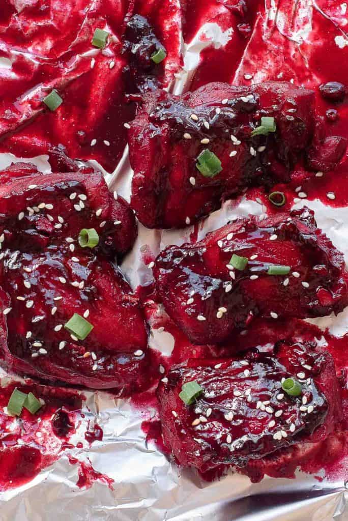 Five pieces of glazed meat with a deep red sauce are topped with sesame seeds and chopped green onions, served on crumpled aluminum foil.