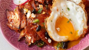Close-up of a plate with chilaquiles topped with black beans, green onions, cheese, and a sunny-side-up fried egg with a runny yolk.