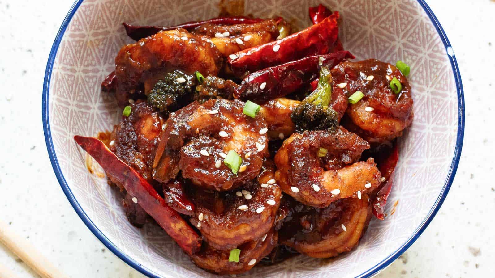 A bowl of spicy shrimp cooked with dried red chilies, garnished with sesame seeds and chopped green onions.