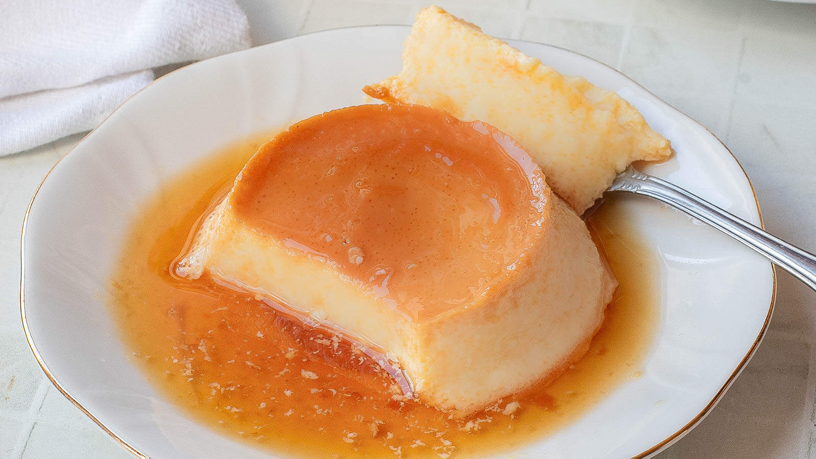 A plate with a serving of Vietnamese Egg Flan, topped with caramel sauce, with a fork holding a piece.