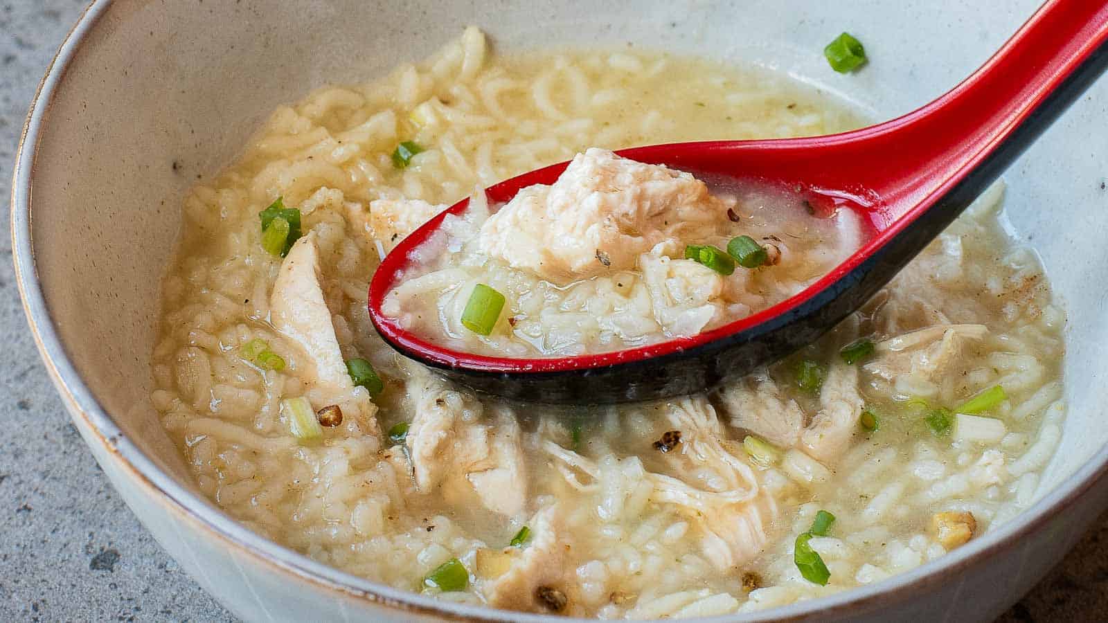 A bowl of chicken and rice soup with chopped green onions, served with a red spoon.