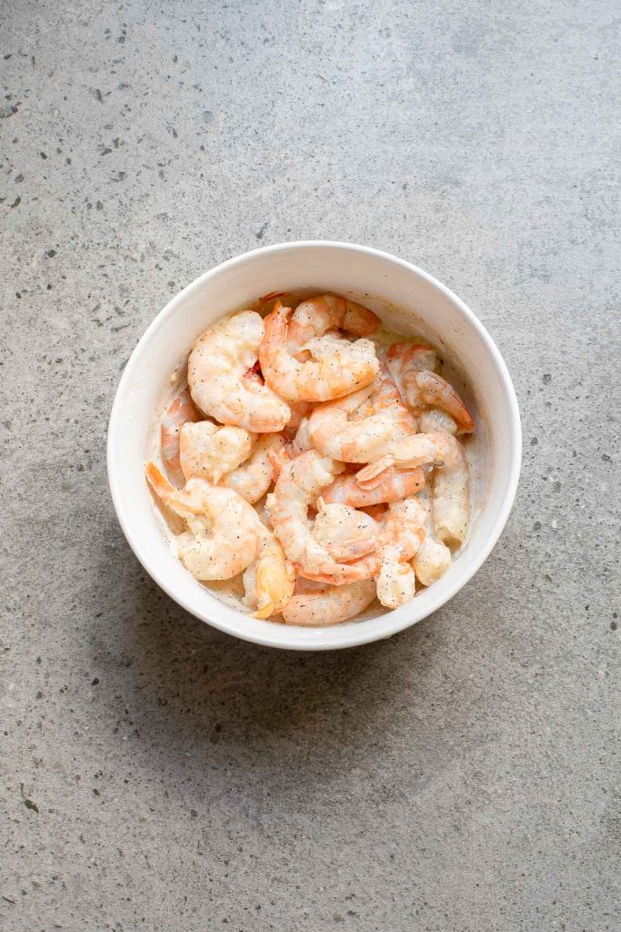 A white bowl filled with cooked, peeled shrimp on a gray speckled surface.