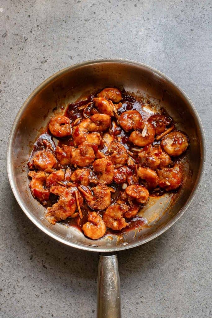 A pan filled with cooked shrimp coated in a reddish-brown sauce sits on a gray countertop.