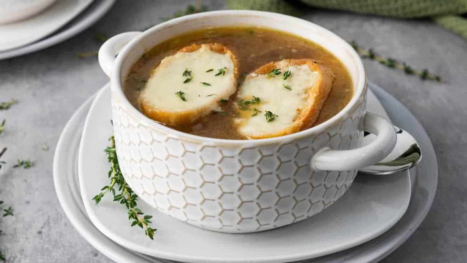 A white soup bowl of French onion soup topped with two slices of toasted bread and melted cheese, garnished with fresh thyme.