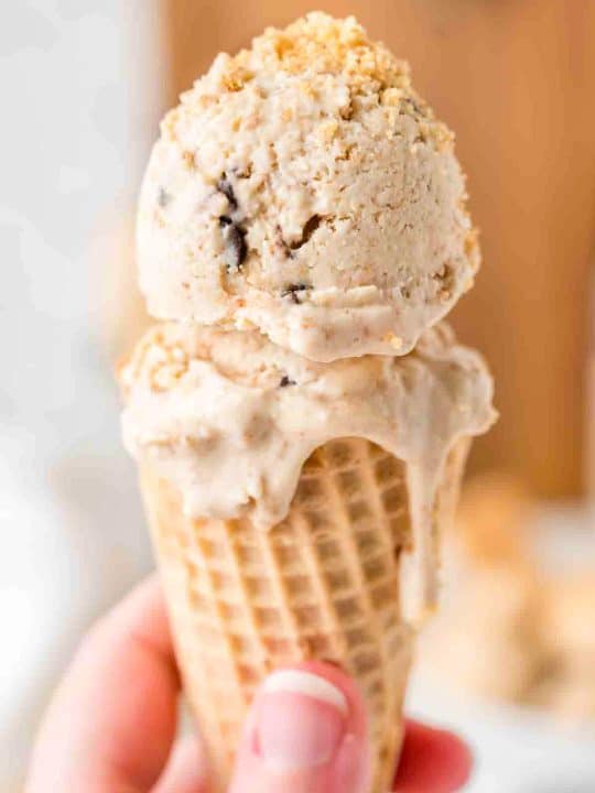 A hand holds an ice cream cone with two scoops of ice cream on top, one scoop slightly melting and dripping down the cone.