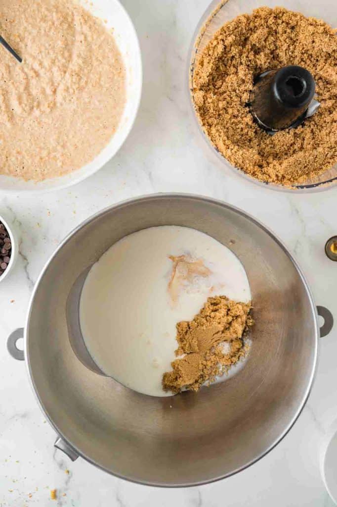 A mixing bowl containing milk and brown sugar next to bowls of wet and dry baking ingredients on a white countertop.
