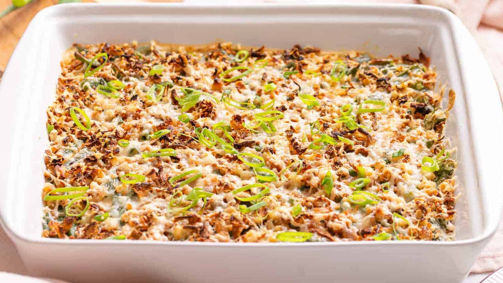 A baked casserole topped with melted cheese, browned bits, and chopped green onions in a white rectangular dish.