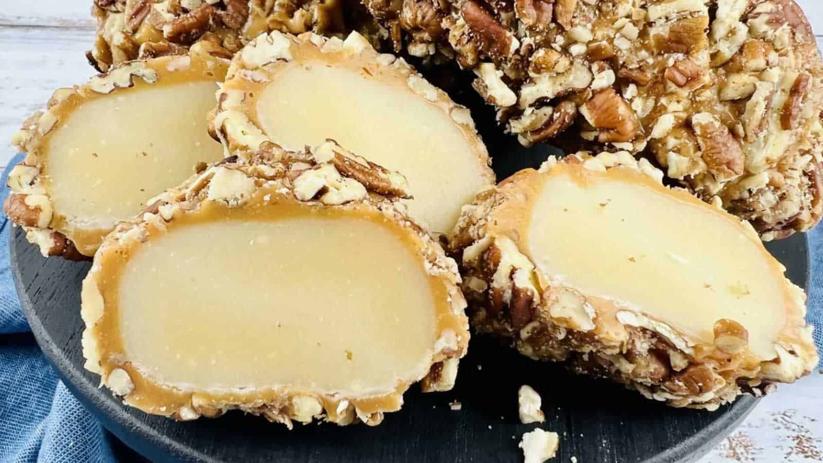 Sliced pieces of pecan-coated candy with a creamy beige filling displayed on a dark round serving board.