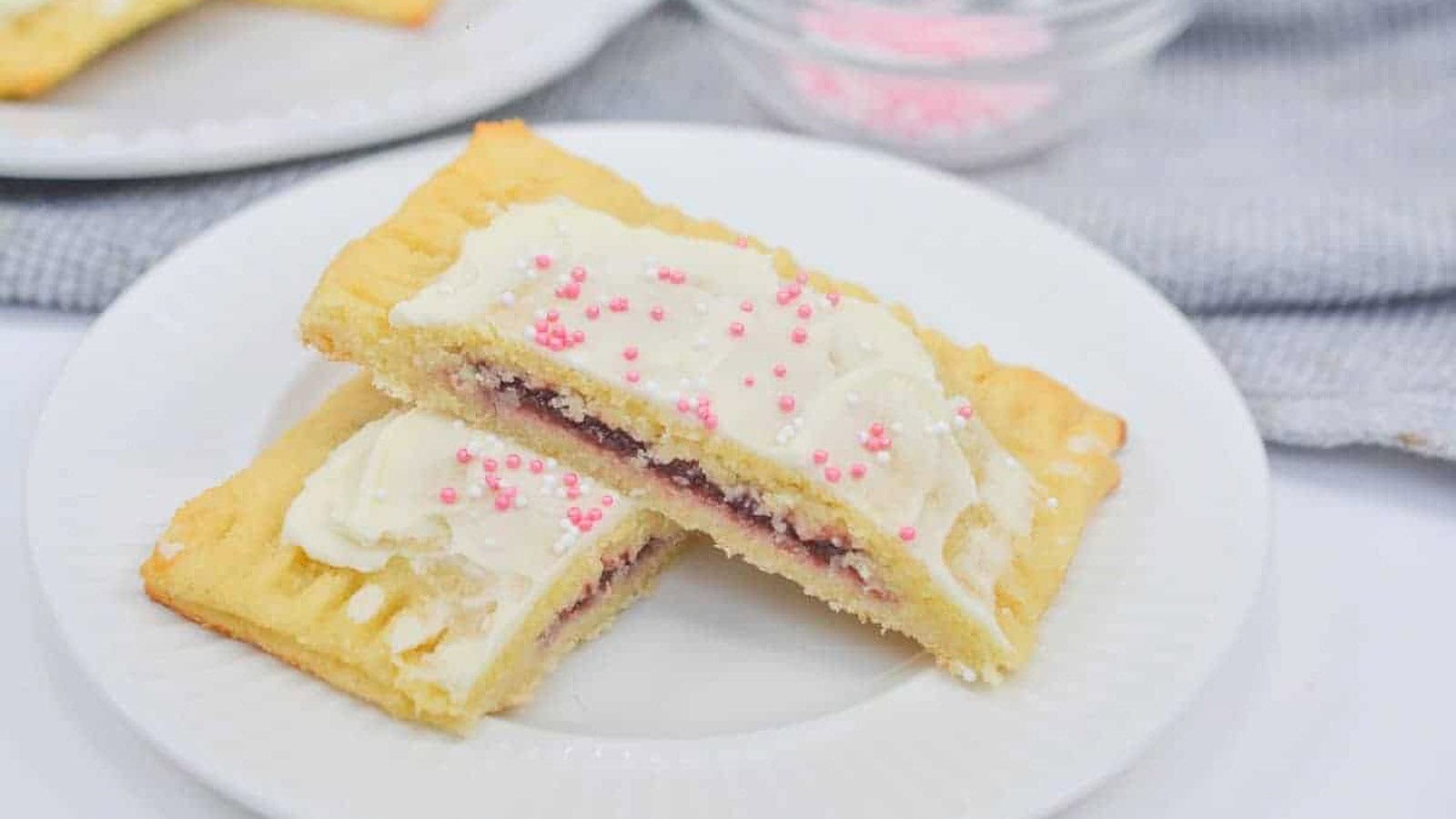 A plate with a slice of a cookie with frosting and sprinkles.