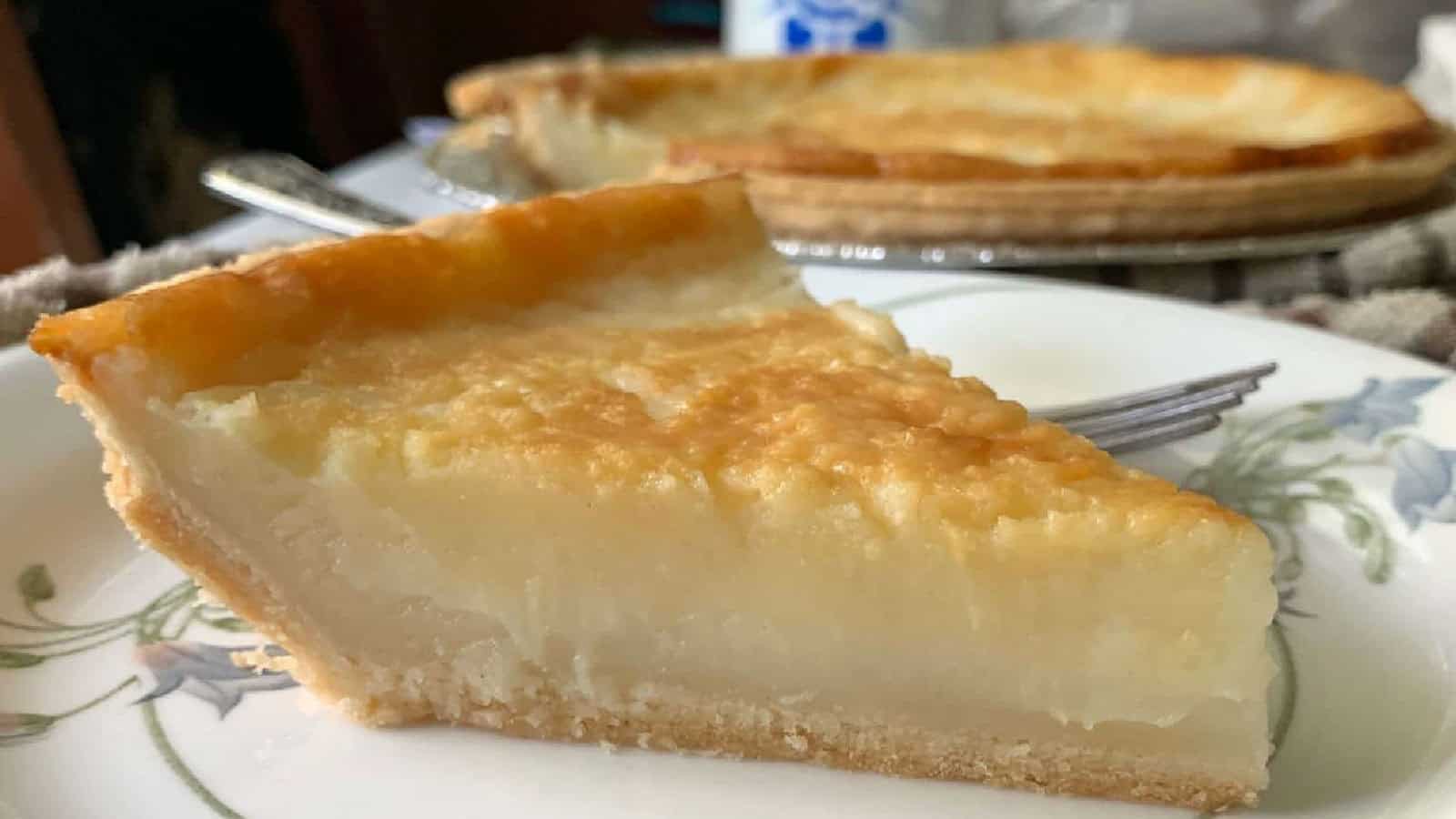 A close-up of a slice of custard pie on a floral plate, with the rest of the pie visible in the background.