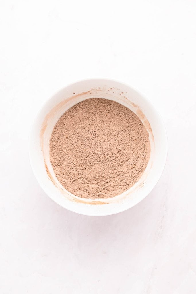 A white bowl filled with dry cocoa powder mixture sits on a white surface.