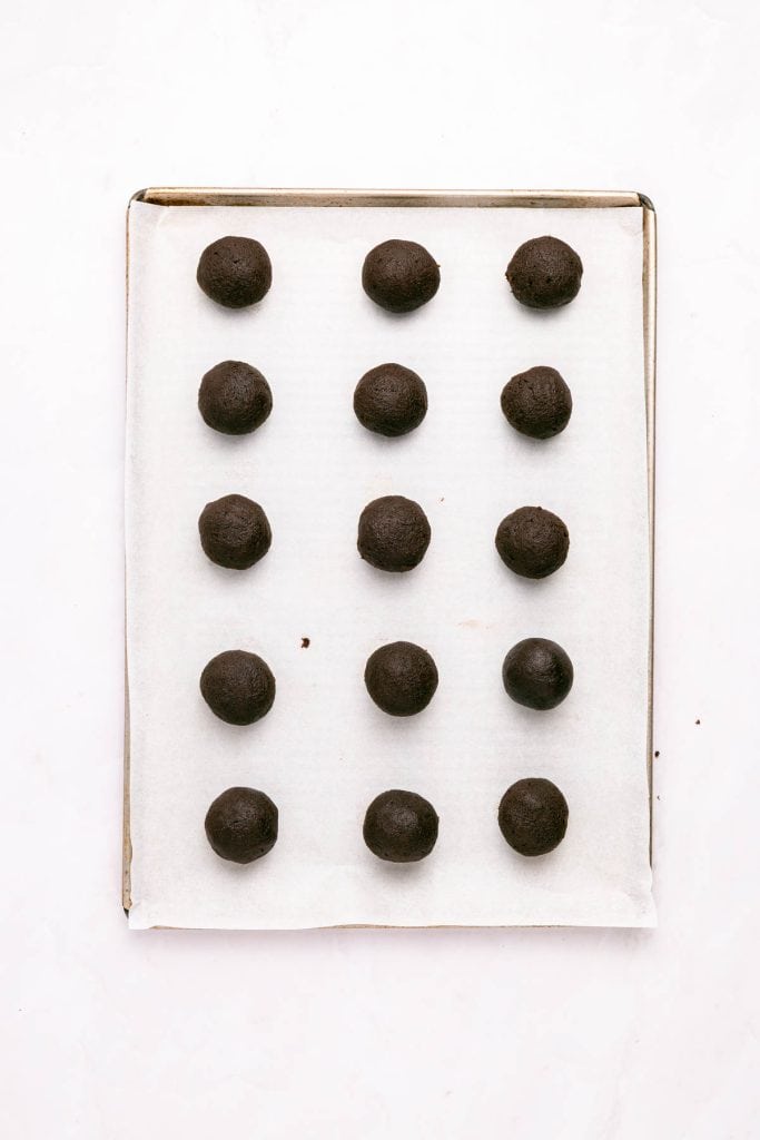 A baking sheet lined with parchment paper holds 12 evenly spaced balls of dark chocolate cookie dough.