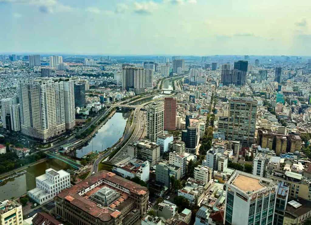 Aerial view of a densely populated urban area with high-rise buildings, roads, and a river running through the city under a cloudy sky.